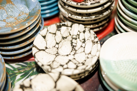 Stacks of decorative ceramic plates feature various intricate patterns and colors, including cracked black and white designs, creating an artistic and vibrant display.
