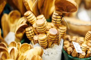 A collection of wooden honey dippers and spoons are displayed in a white lace-trimmed container. The polished wood has a warm, natural tone, creating a rustic feel.