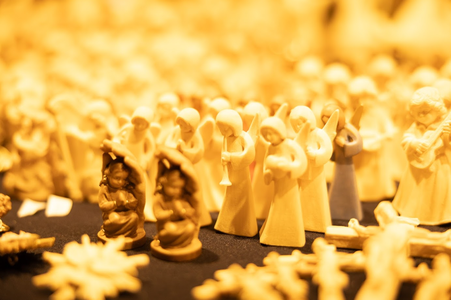 A warm, golden-hued image of small, carved angel figurines and nativity scenes displayed closely together. The setting conveys a festive, peaceful atmosphere.
