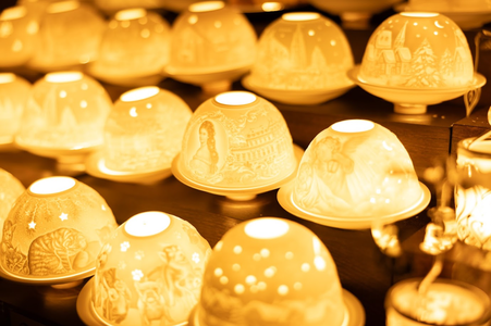 Rows of intricately carved, glowing porcelain tealight holders emit a warm, golden light. Each dome displays detailed, decorative scenes, creating a cozy ambiance.