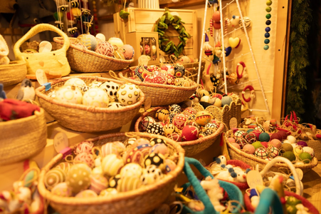 Baskets filled with colorful, patterned felt balls displayed on shelves at a cozy, warm-toned craft market booth, creating a festive atmosphere.