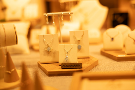 Display of elegant aquamarine necklaces with intricate designs in a warmly lit jewelry store. The scene exudes luxury and sophistication.