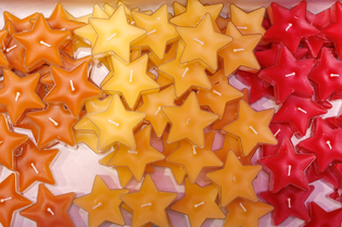 Star-shaped candles in vibrant shades of orange, yellow, and red are clustered together. The warm tones create a cozy, festive ambiance.