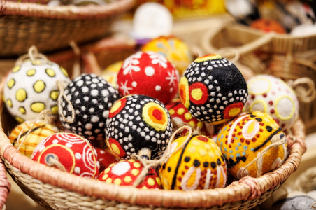 Colorful felt balls with vibrant patterns fill a woven basket. The balls display a mix of polka dots, stars, and swirls in red, black, and yellow.