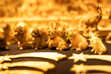 Small ceramic animal figurines, including dogs and pigs, are displayed on a black surface. Golden shooting star ornaments are in the foreground. Warm lighting.