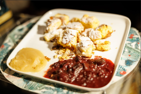 A white plate holds powdered sugar-dusted, bite-sized pastries, with a dollop of smooth applesauce and rich berry compote, creating a cozy, inviting scene.