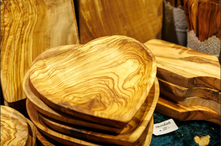 Heart-shaped olive wood bowls stacked on a table, showcasing intricate wood grain patterns. The warm tones create a cozy, artisanal feel. Price tag visible.