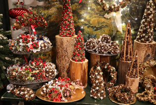 A festive display of handcrafted Christmas decorations, featuring pinecone wreaths and trees adorned with ribbons and lights, set on wooden logs.