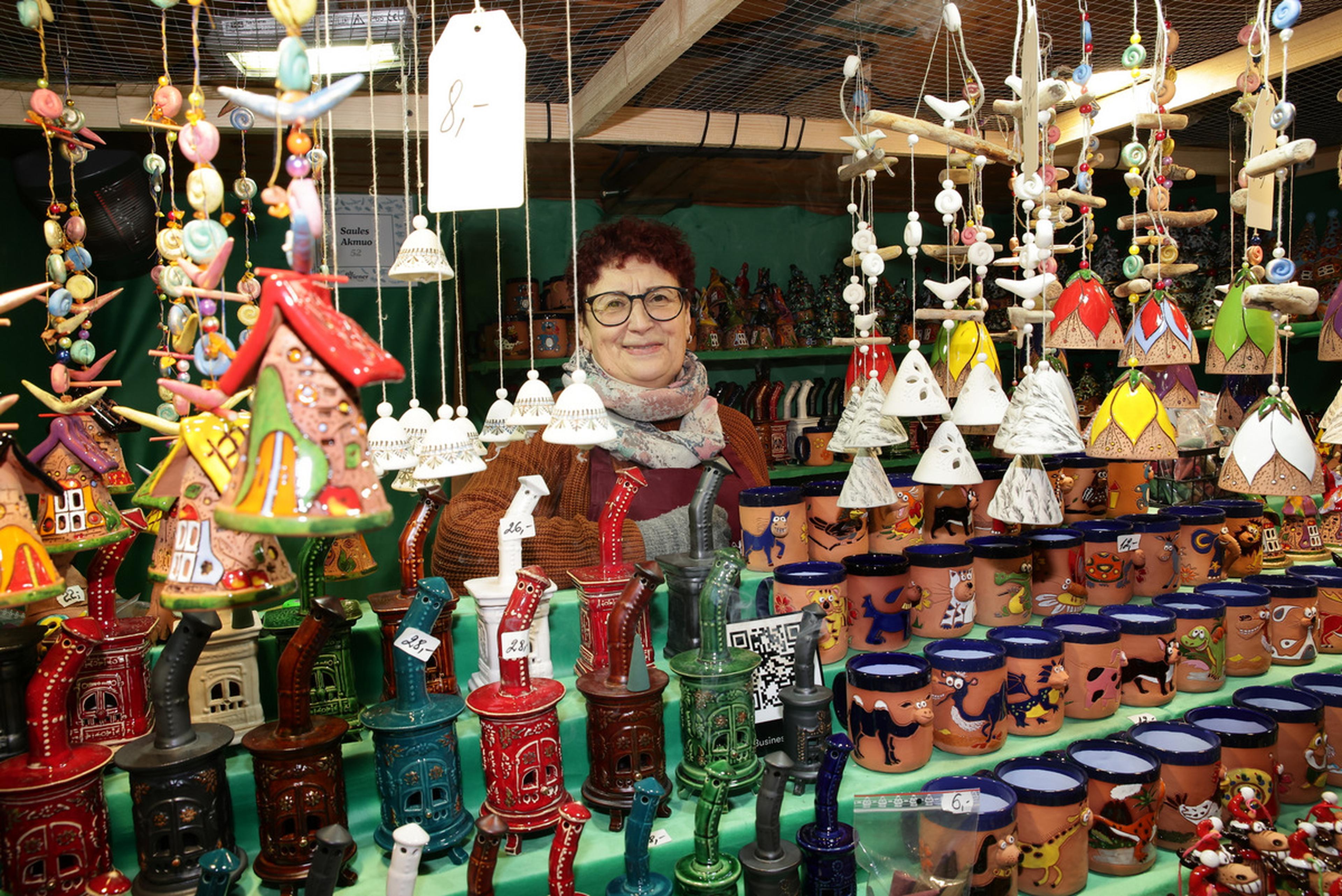 A person stands behind a colorful display of handcrafted pottery and decorative items at a market stall, surrounded by hanging ornaments.