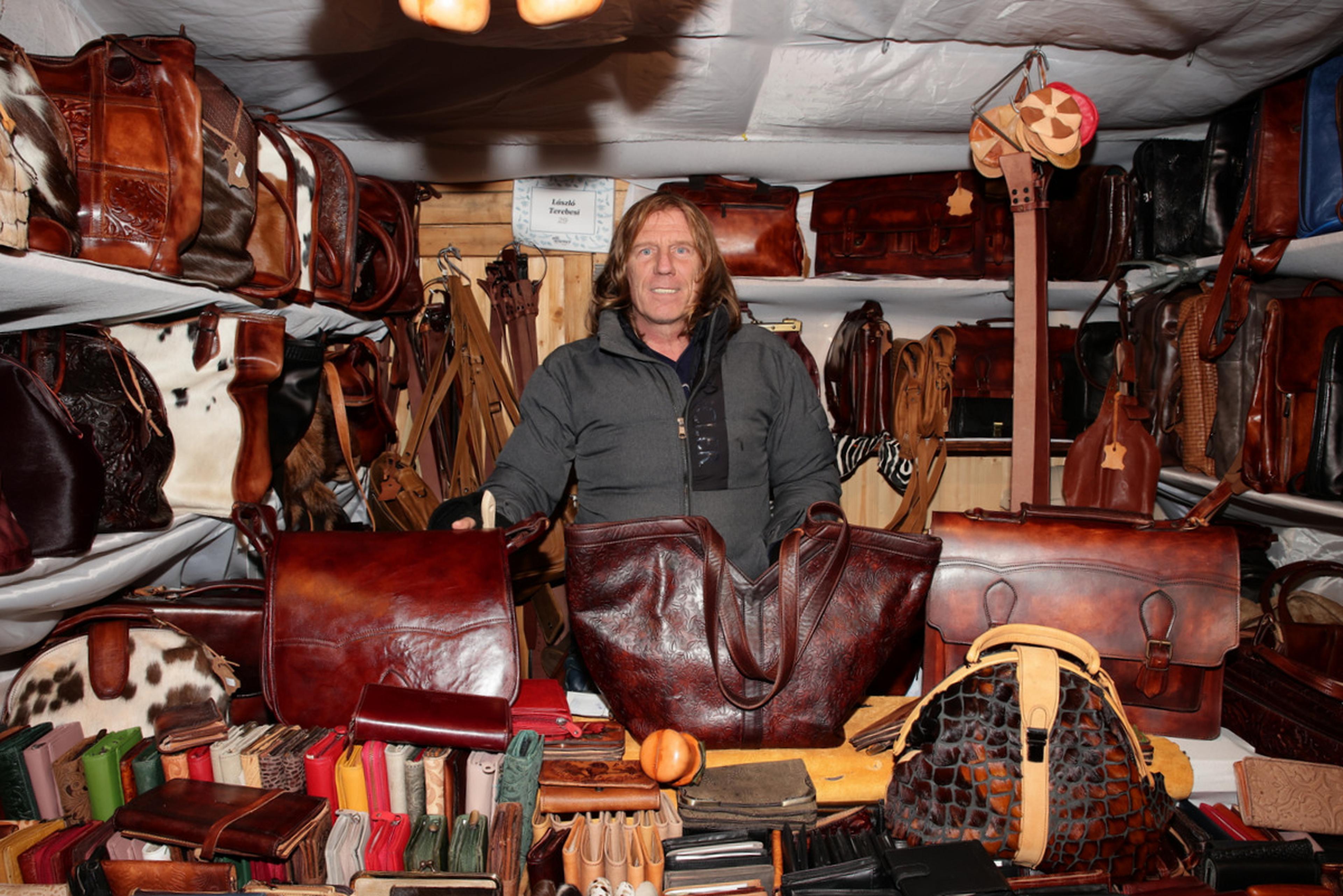 A person stands in a leather goods stall, surrounded by various bags, wallets, and accessories, with shelves filled with products.