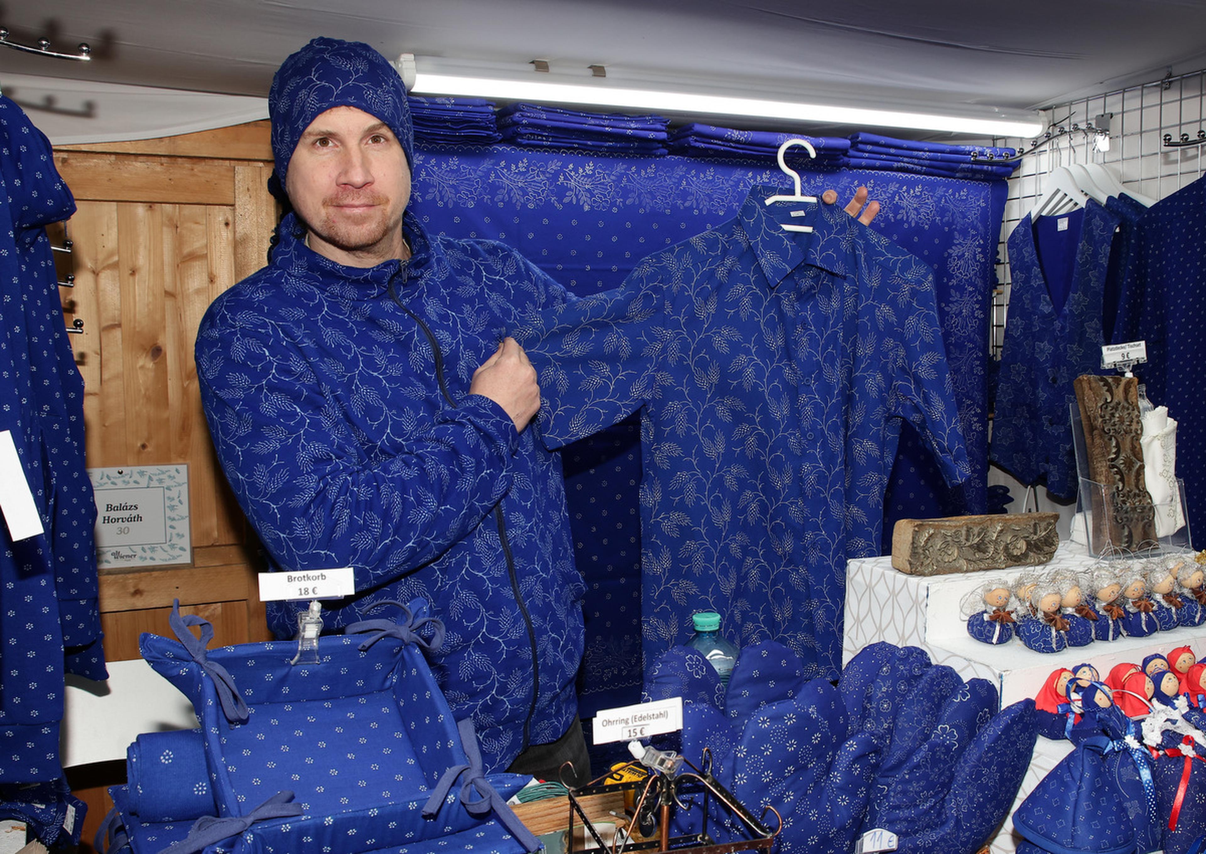 A person wearing a blue patterned outfit showcases a matching blue shirt in a shop filled with similar blue garments and accessories.