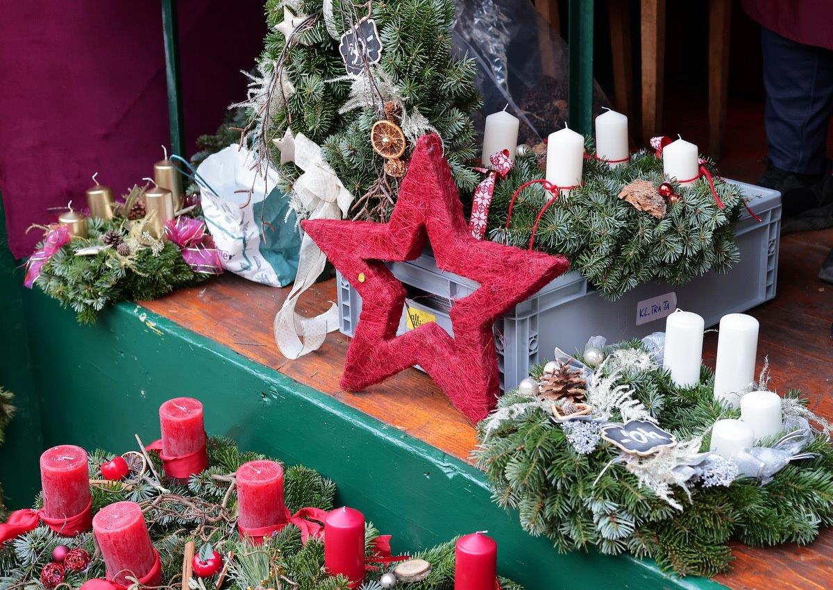 Christmas wreaths adorned with red and white candles, pine cones, and a large red star displayed on a wooden surface.