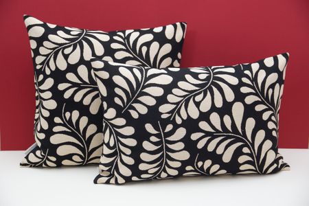Two decorative pillows with black and white leaf patterns, placed against a red background.