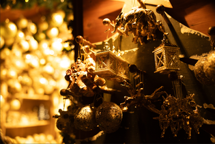 Close-up of festive gold and bronze Christmas ornaments, including baubles and lanterns, hanging against a warm, glowing background.