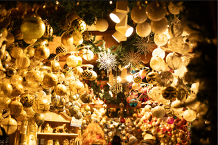 A festive market stall filled with various colorful Christmas ornaments, glowing warmly under decorative lights and evergreen garlands.
