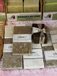 Various handmade soaps displayed, including brown and beige bars labeled "Ottoman." Some are wrapped, with a wooden soap dish nearby.
