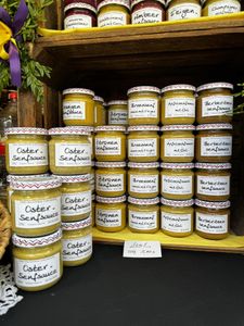 Jars of various flavored sauces and mustards are neatly stacked on wooden shelves at a market display.