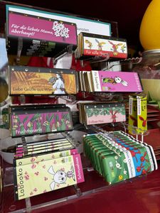 Display of colorful chocolate bars with various whimsical designs and German text, arranged in a tiered stand.