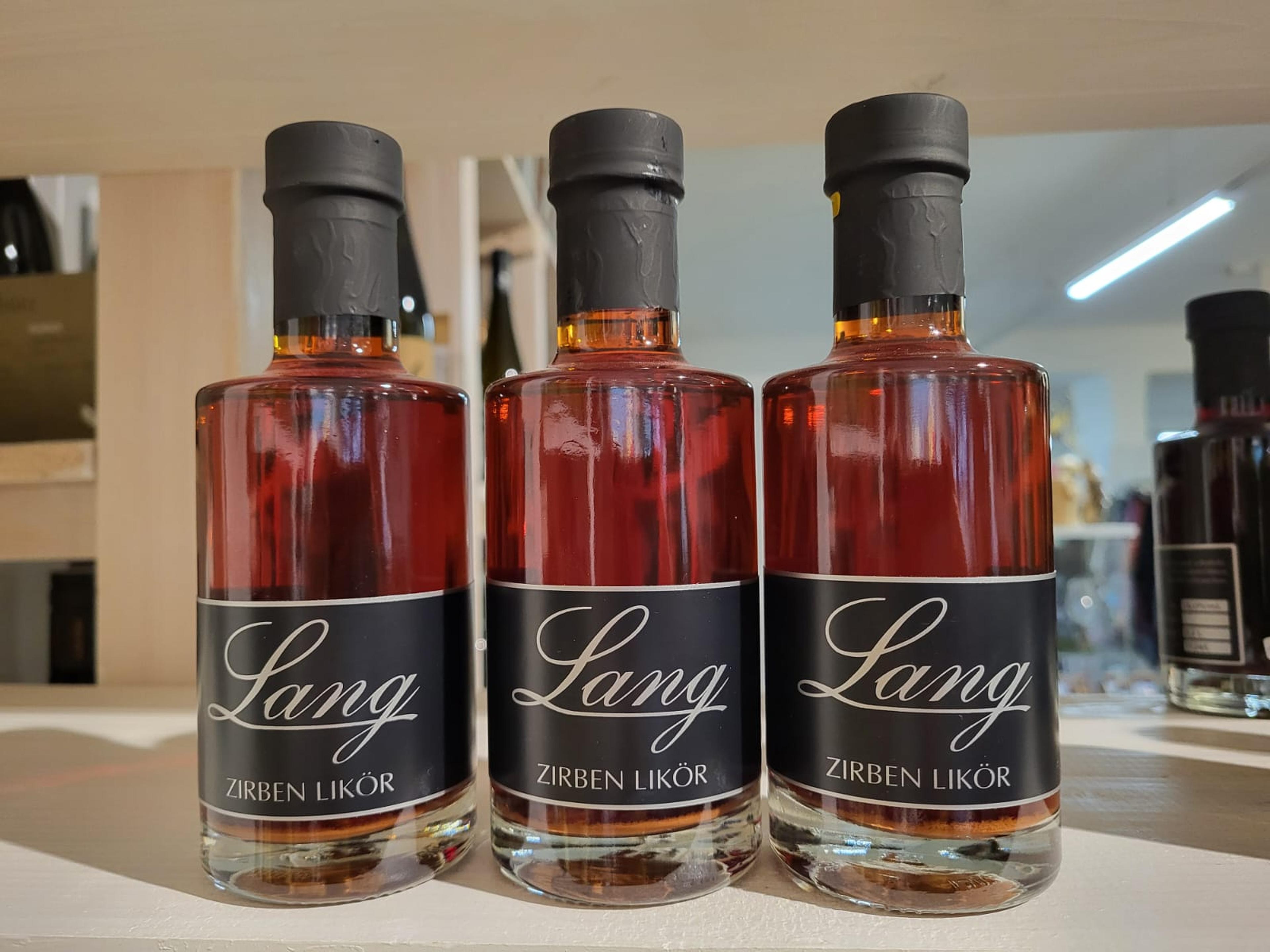 Three bottles of Lang Zirben Liqueur with black labels and gold caps are displayed on a shelf in a well-lit store.