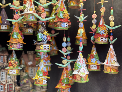 Colorful, miniature ceramic houses with whimsical designs and intricate details are hanging on strings, displayed on a dark background.