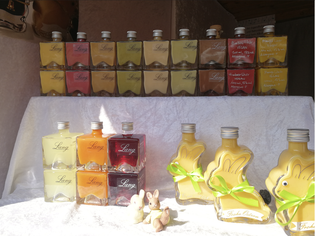 Bottles of colorful liqueurs in cube and bunny-shaped bottles displayed on shelves with decorative ornaments in front.