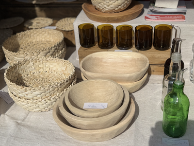 Woven baskets, wooden bowls, amber glasses, and green bottles displayed on a sunlit table with a white cloth.