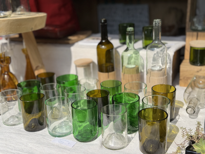 A collection of recycled glassware, including green and clear glasses and bottles, displayed on a table in sunlight.