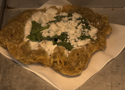 A fried dish topped with cream, fresh green leaves, and crumbled cheese on a paper napkin.