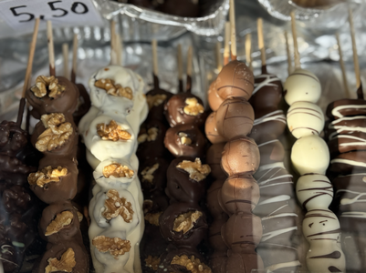 Various chocolate-covered skewers topped with walnuts and white chocolate drizzles are displayed for sale.
