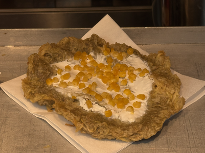Deep-fried flatbread on a napkin, topped with sour cream and scattered corn kernels.