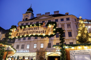 Festive Christmas market entrance with fairy lights and decorations, set against a historical building at dusk.