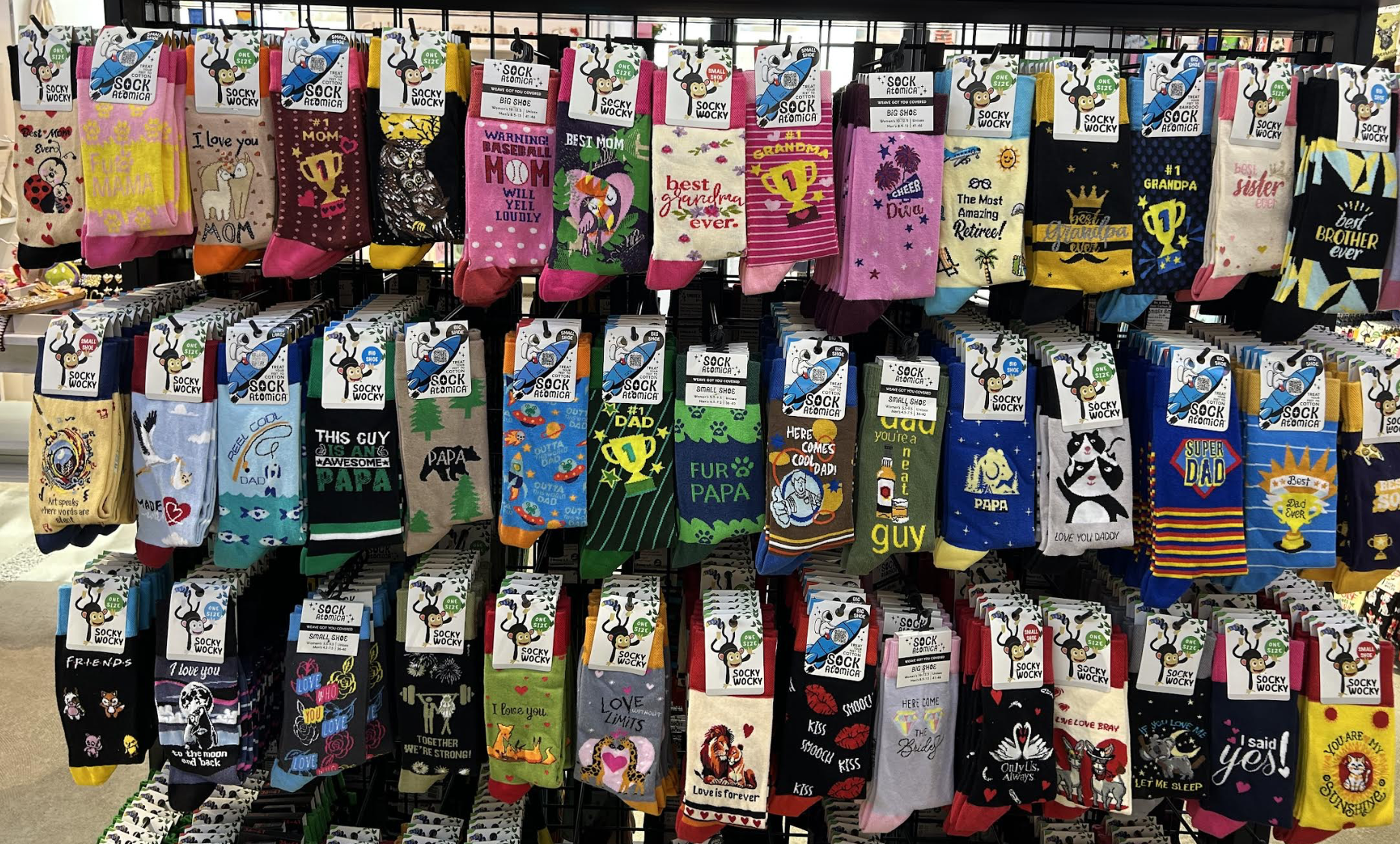 A display of colorful novelty socks with various designs and humorous messages, neatly organized on a black grid rack.