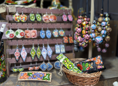 A display of colorful, hand-painted floral jewelry and accessories, featuring earrings and necklaces, with a wicker basket holding small items.