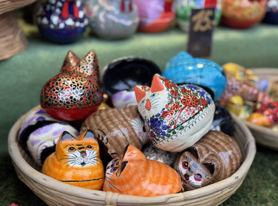A woven basket filled with colorful, painted ceramic cat figurines, each uniquely decorated with intricate patterns and vibrant colors.