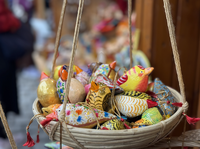 A basket filled with colorful, handcrafted bird ornaments, each adorned with intricate patterns and vibrant hues, hangs from ropes.