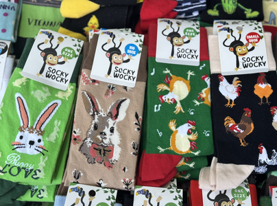 Colorful "Socky Wocky" socks displayed. Designs feature rabbits and chickens on green, brown, and black backgrounds. Labels indicate one size and big or small shoe options. Playful and whimsical tone.