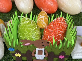 Colorful eggs, crafted with a textured finish, sit in a grass-like basket adorned with a bunny decoration, evoking a festive and cheerful mood.