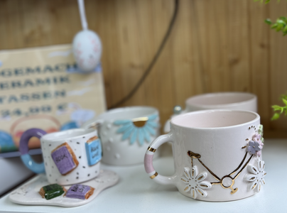 Decorative ceramic mugs displayed on a shelf, featuring floral and geometric designs in pastel colors, creating a cozy and artistic ambiance.
