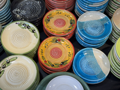 Colorful ceramic plates stacked in rows display vibrant designs, including olives and abstract patterns, conveying a lively, artistic atmosphere.