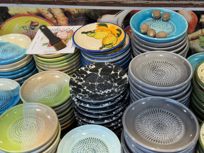 Stacks of colorful ceramic plates with intricate patterns fill the image. A yellow fruit design decorates one plate; three nutmegs rest on another.