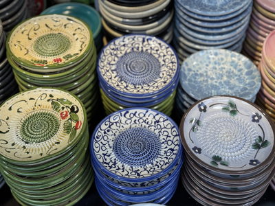 Stacks of decorative ceramic plates, each featuring intricate patterns and floral motifs in diverse colors, are displayed in rows, evoking a vibrant and artistic ambiance.
