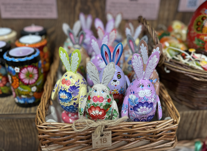 A basket of colorful, decorative rabbit and egg figurines with floral patterns, displayed on a wooden table.