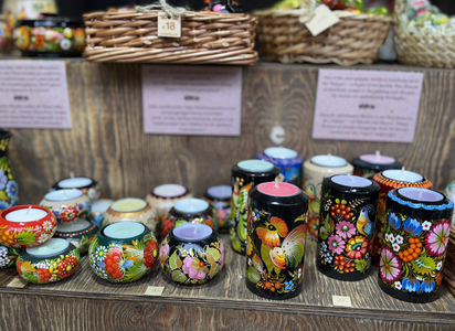 Colorful, hand-painted pottery with floral and bird designs displayed on a wooden shelf, surrounded by woven baskets.