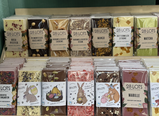 Various flavors of 28 LOTS chocolate bars in clear packaging on display, featuring unique ingredients like matcha, mango, and sesame.
