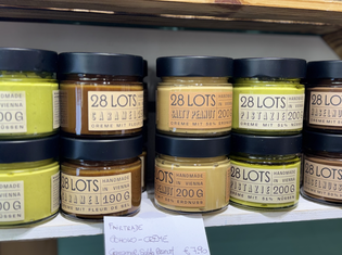 Jars of handmade nut spreads, including caramel, salty peanut, and pistachio, displayed on a shelf with price tag.