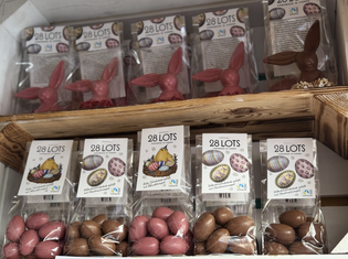 Shelves display packaged chocolate bunnies and eggs, labeled "28 LOTS," with colorful Easter designs and Fairtrade certification.