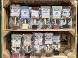 Wooden display with two shelves of packaged chocolate sticks. Each stick has a different flavor, like vanilla and ruby, labeled "28 LOTS." Colorful and inviting.