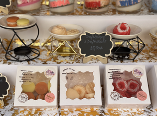 Assorted colorful soaps resembling macarons and whipped cream displayed in decorative packaging and plates.