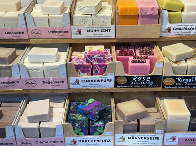 Colorful handmade soaps displayed in a wooden rack, labeled with various creative names, such as "Einhornpups" and "Drachenfurz."