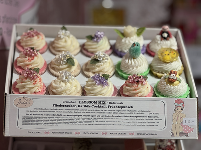 A box of decorative cupcake-shaped bath bombs, each topped with colorful floral and fruit designs, labeled "Blossom Mix."